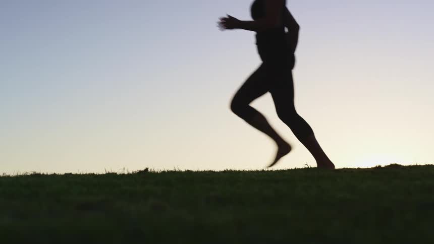 The silhouette of a woman runs through an open field in the early morning