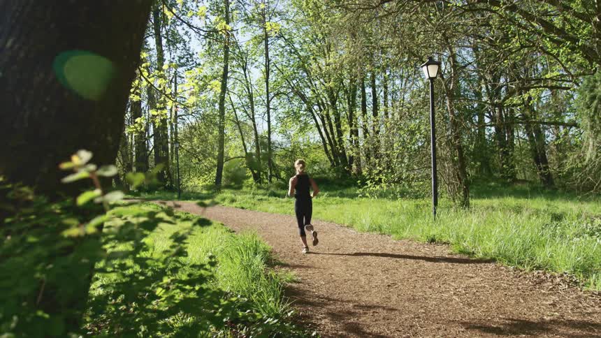 A woman running on a dirt path surrounded by grass and trees with the sky in the background