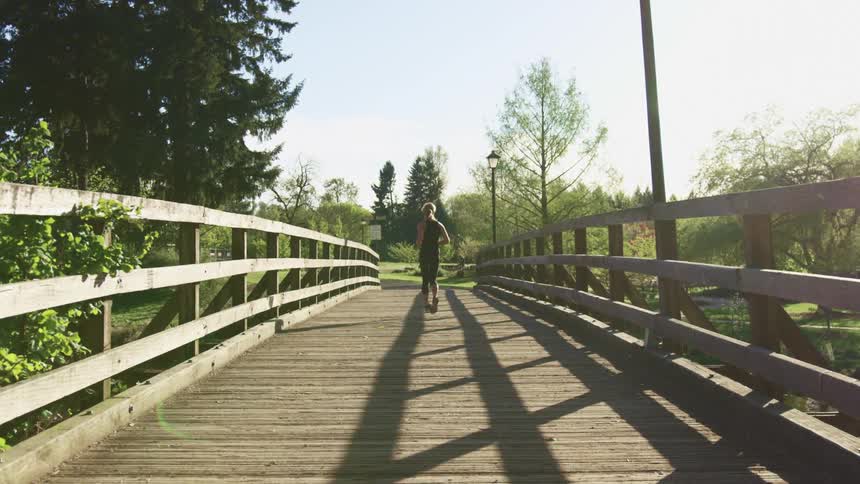 Woman with a ponytail black tights and running shoes runs across a timber bridge on a sunny day
