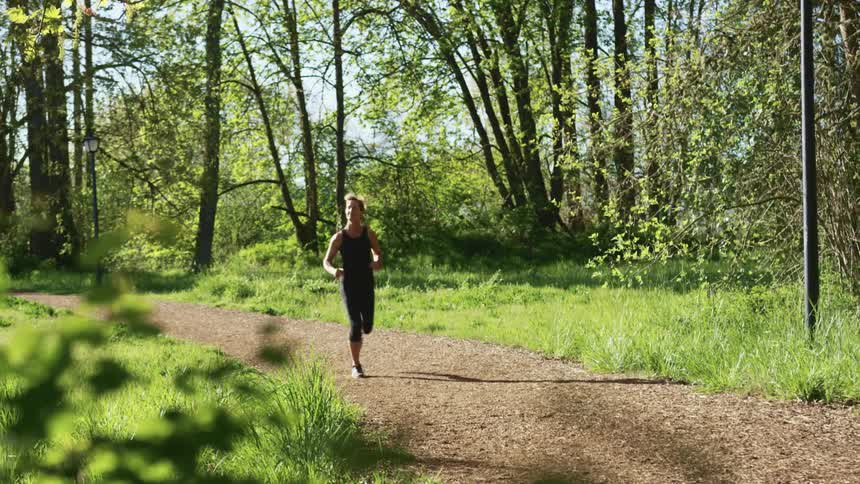 Woman with a ponytail tights and a pair of shoes jogs along a dirt road in the forest