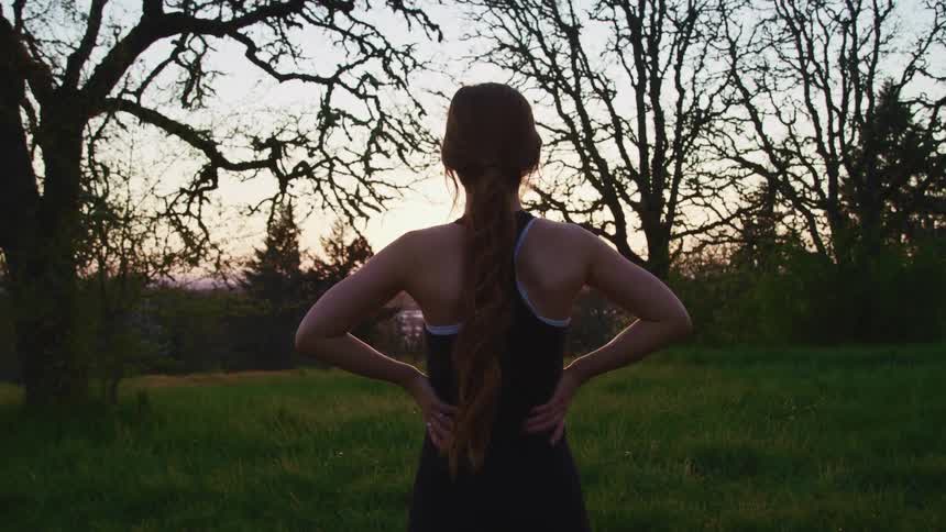 A woman stands outside and looks towards the trees