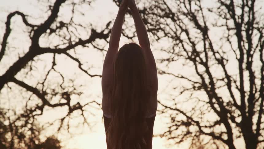 Woman wearing sports clothing practices yoga outdoors at sunset