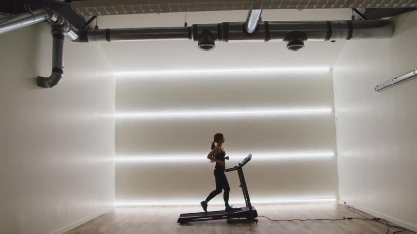 Woman with a ponytail and black tights runs on a treadmill in a room