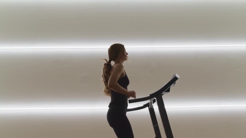 Woman with a ponytail and black tights runs on a treadmill in a room