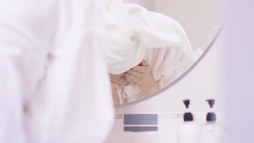 Woman washes face in front of round mirror