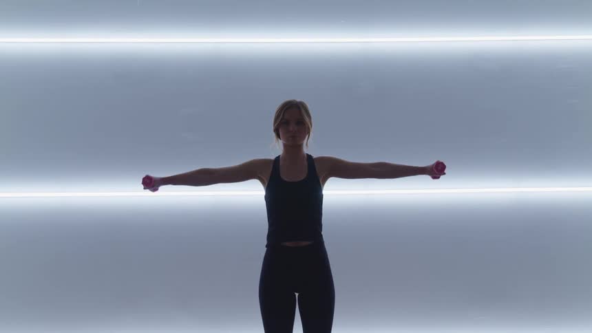 A woman lifts small weights to her sides