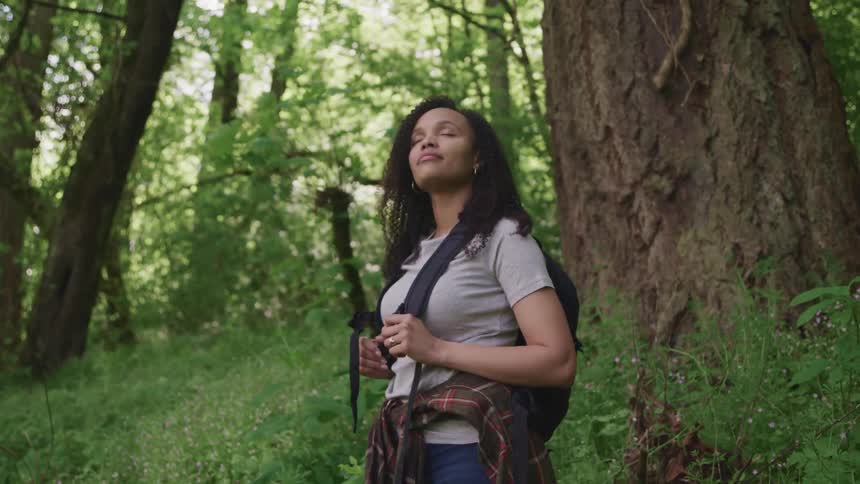 A woman in the forest stands with her eyes closed