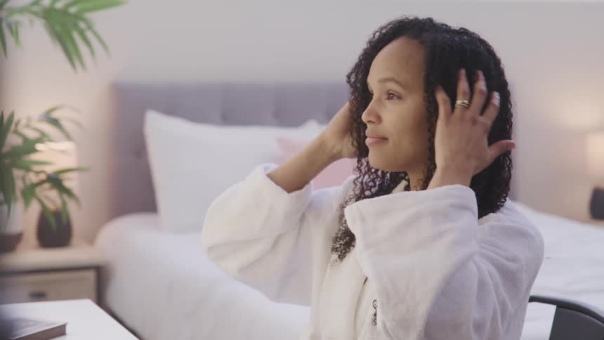 Woman wears robe while styling her hair in the bedroom