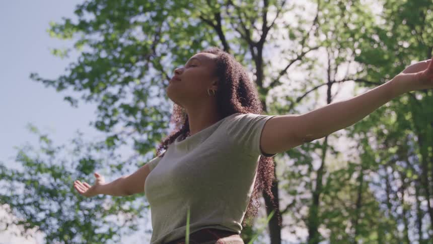 A woman under large trees with her arms stretched out to her side