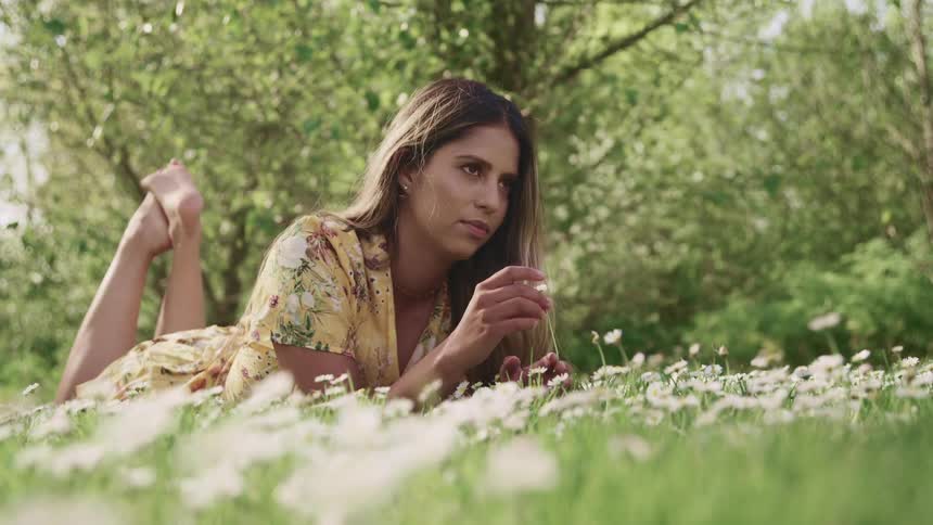 Woman wearing a dress lays on her stomach in a field of flowers and holds one of the flowers