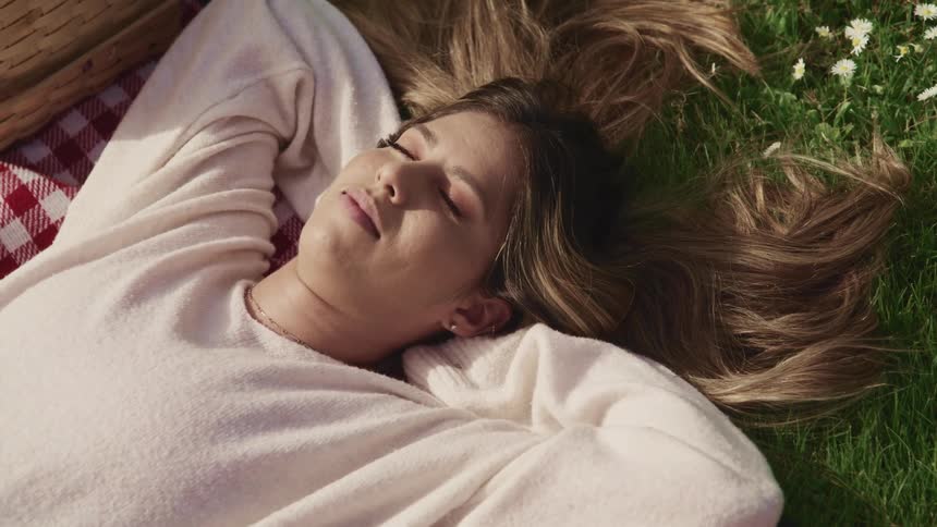 A teenage girl sleeps on a blanket on the grass