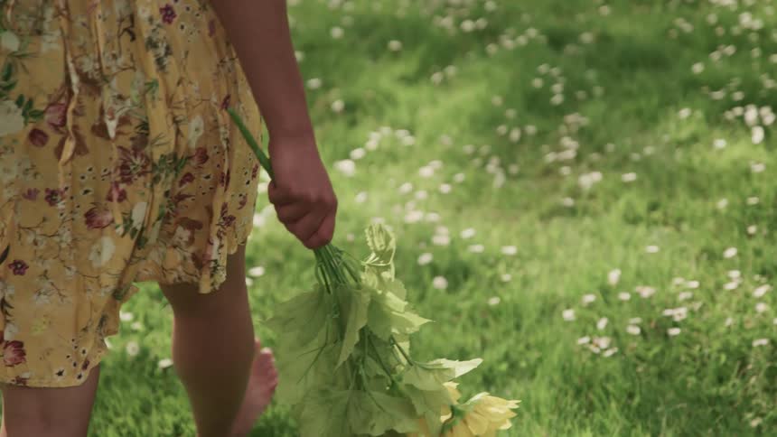 Woman walks barefoot in a field as she carries a floral bouquet