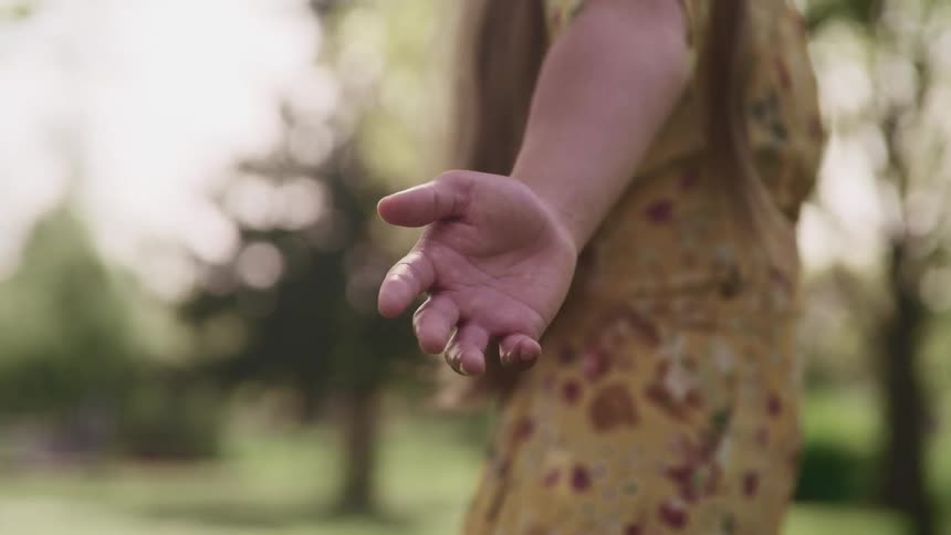 A woman stands outdoors in a field during the day with her arms held wide
