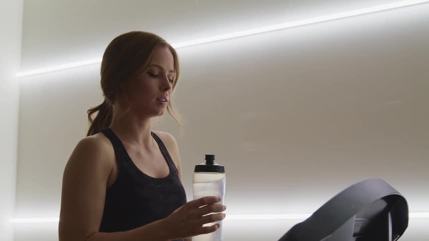 Woman drinks water from a transparent plastic bottle after exercising
