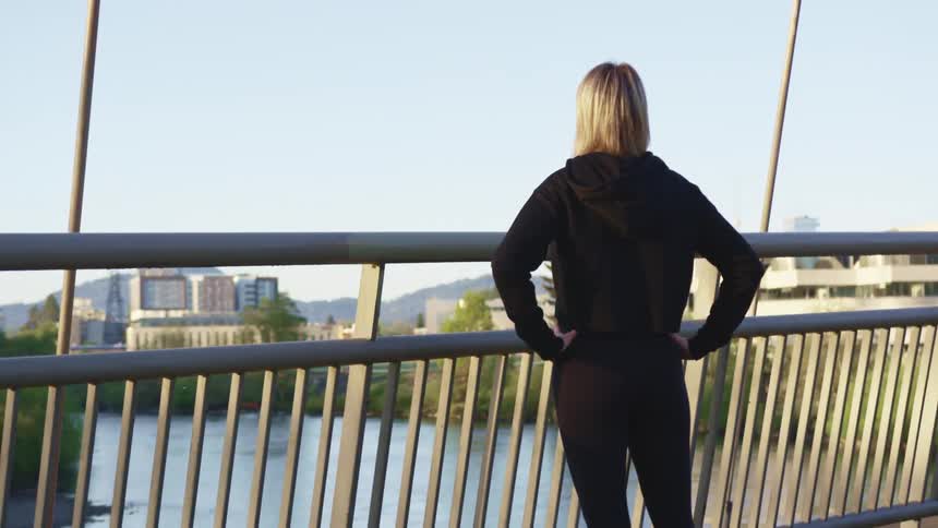 A woman standing on a bridge looks across the water and towards the city skyline