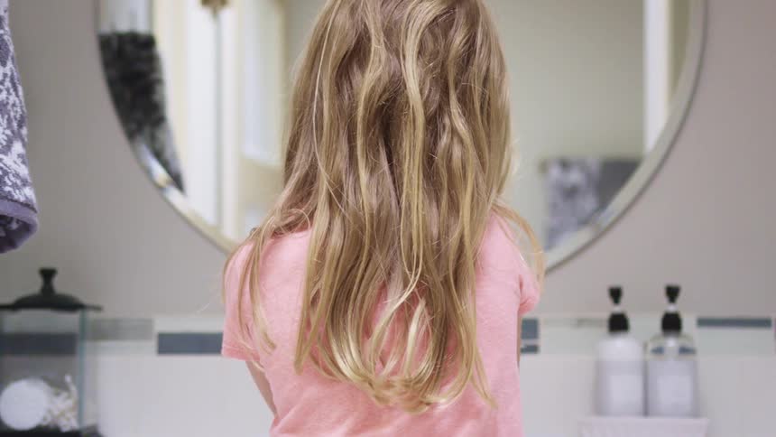 A young girl washes her hands in a bathroom sink