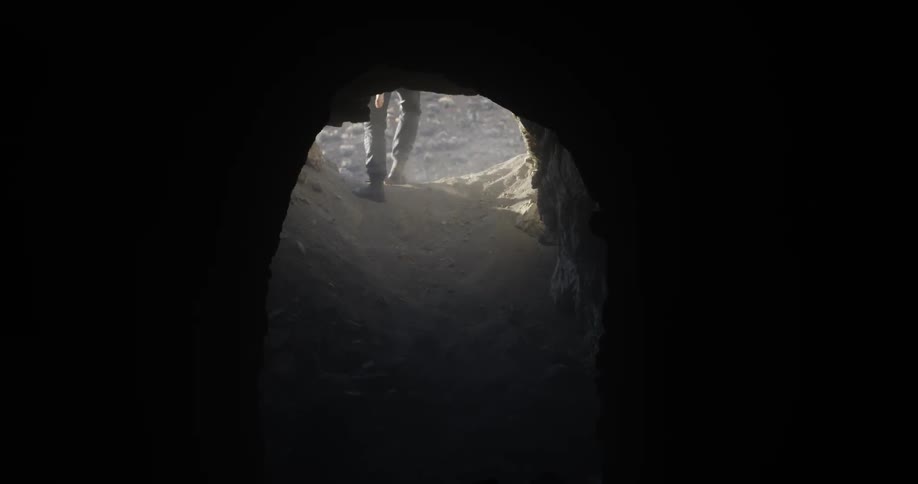 A man carrying a child on his back climbs out of an underground cave