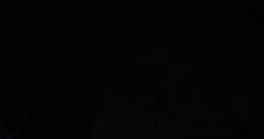 A person is climbing around rocks in a dark cave with a flashlight