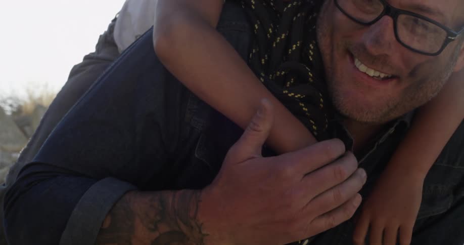 A man smiles while a child hangs from his back