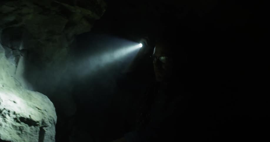 A man explores a dark cave with a flashlight