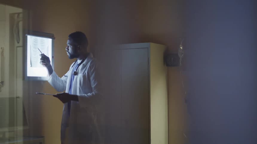 A doctor examines an xray on the wall of a patients room
