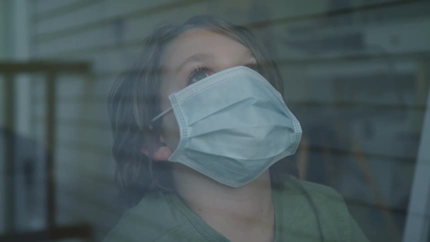 Boy with long hair and a white mask looks out the window