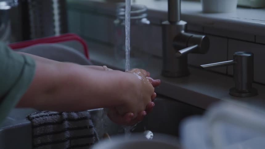 A child washing their hands at a kitchen sink