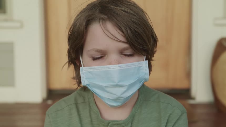 Boy with blue eyes and a mask faces the camera with eye contact
