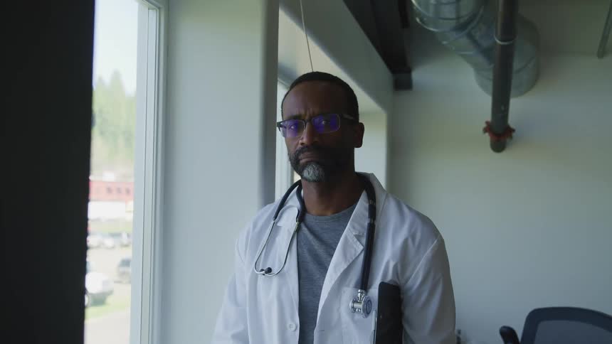 Doctor wearing a white coat and stethoscope looks at the camera