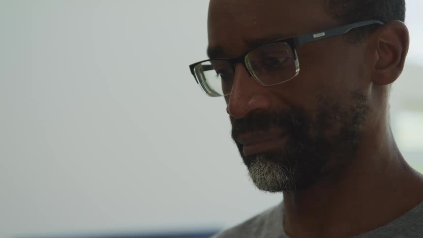 Side view of a black man with beard and glasses looking down