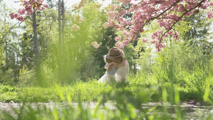 A mother and daughter hugging while sitting on grass