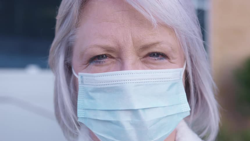 Woman wears face mask outdoors next to building