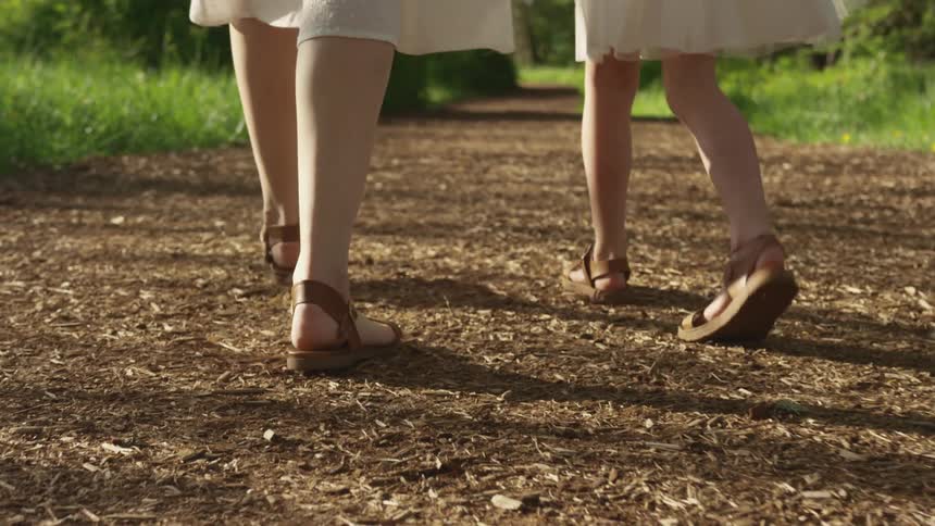 Woman and young girl walk on a trail on a sunny day while wearing sandals
