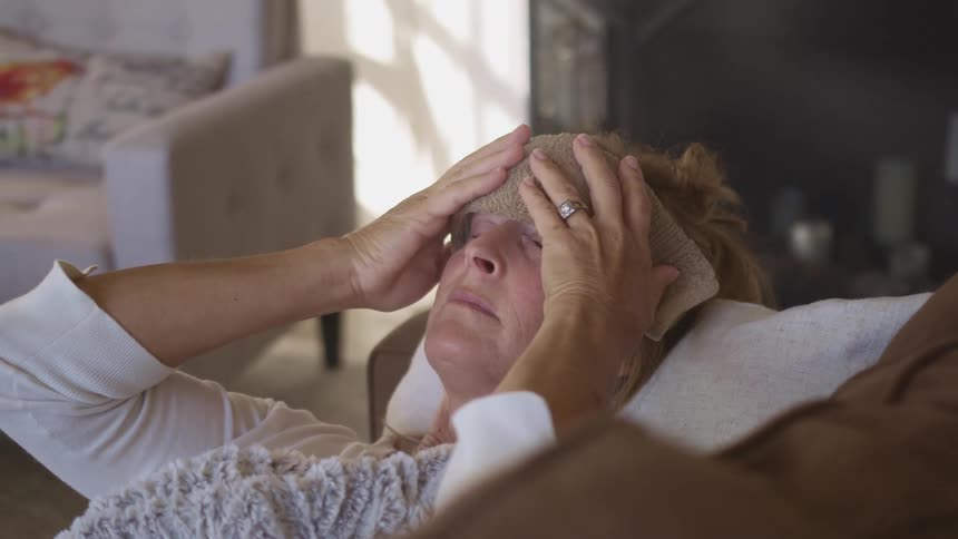 Woman puts towel on her forehead while resting in the couch on the living room