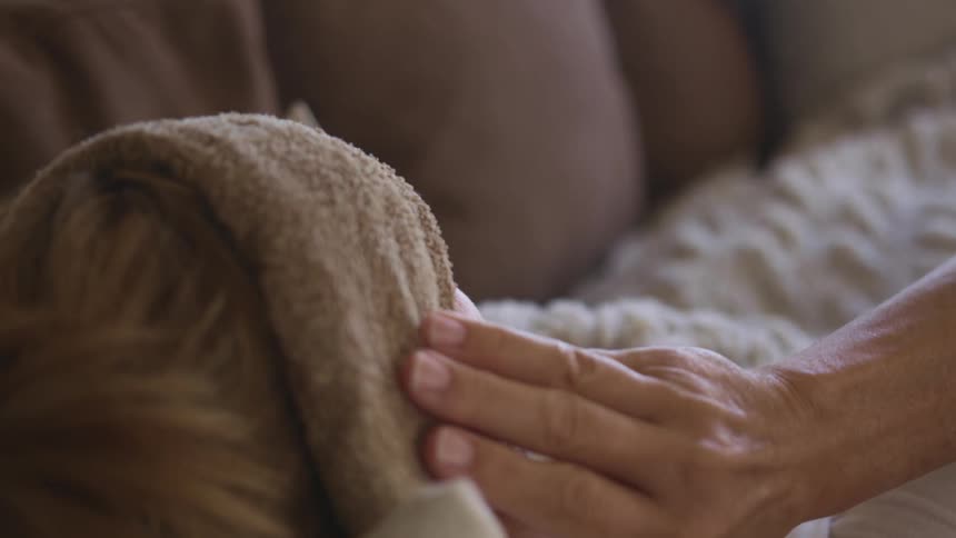 A woman lying on her couch puts a cloth on her forehead