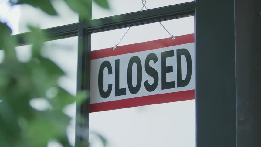 A person flips the open sign hanging in the window of a business to the side that reads closed