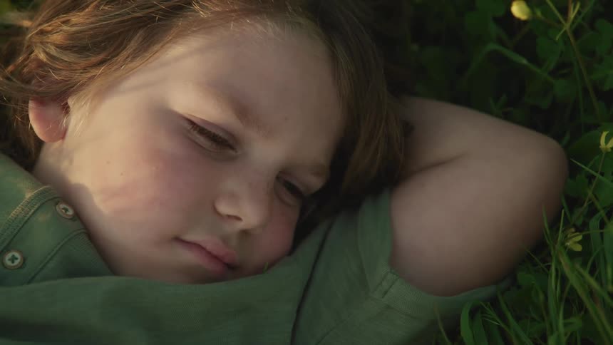 Boy with long hair and a green t shirt lies on green grass