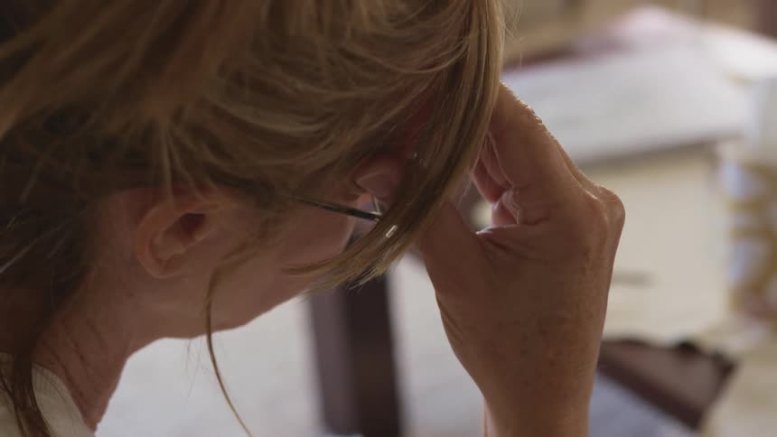 A woman shakes her head side to side while rubbing her forehead in frustration