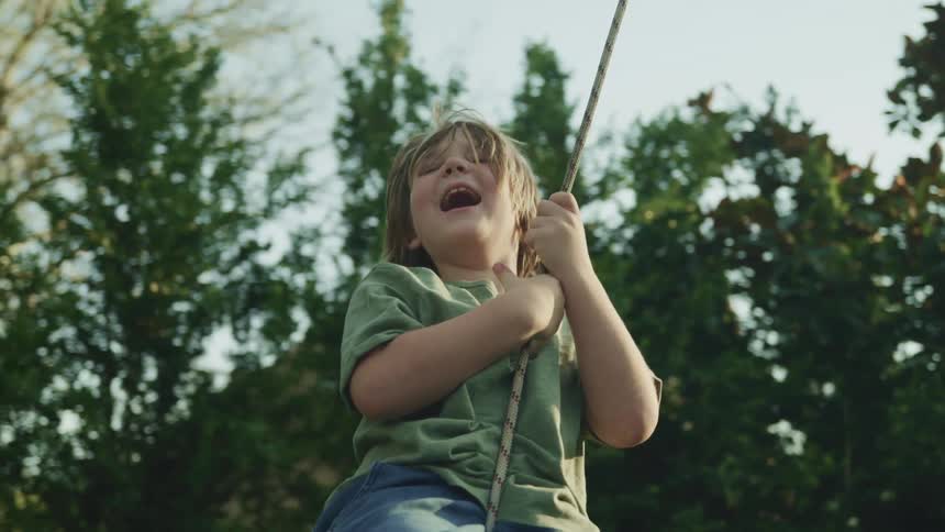 A boy swinging on a rope with trees and the sky in the background