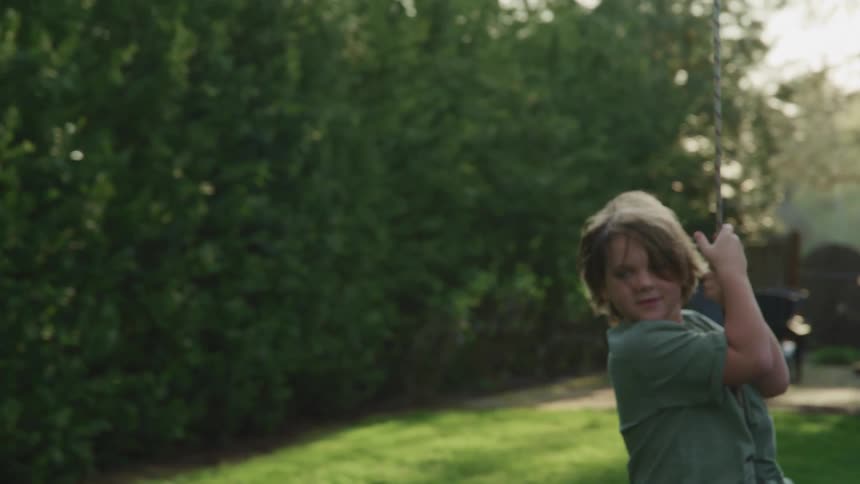 Young boy playing in a swing hanging from a tree in the backyard