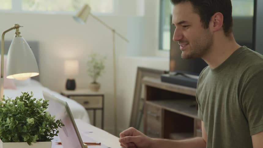 A young man sitting at a desk in his bedroom video chats on his laptop