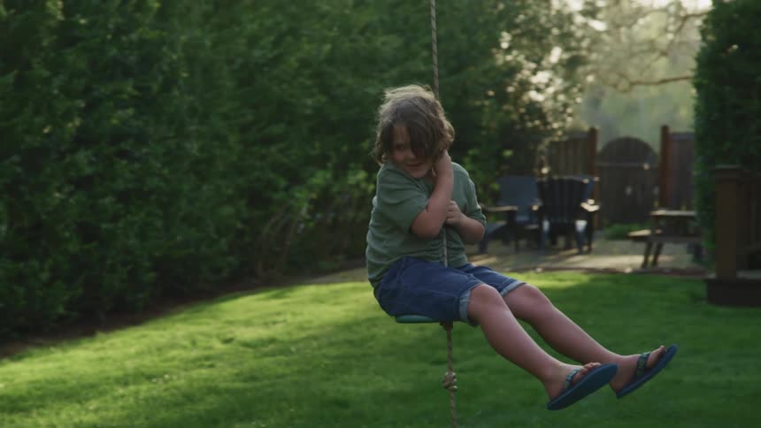 Young boy swings on a backyard swing hanging from a tree