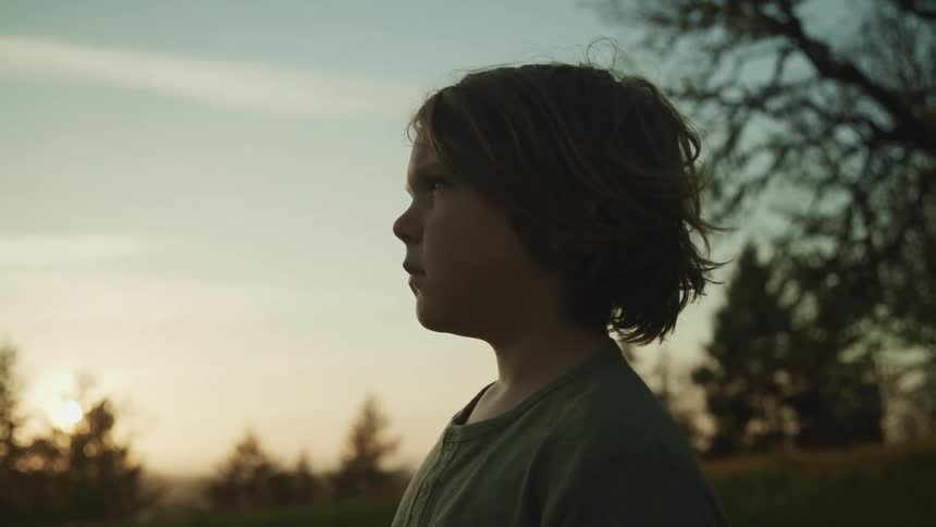 A boy standing with trees the sky and clouds in the background