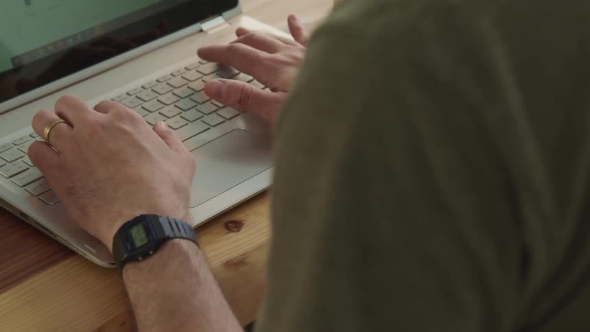 A man types on his laptop at a wooden desk