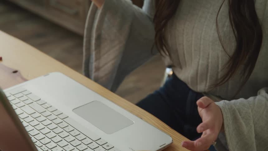 Female sits at desk in front of a laptop while video chatting and talking with her hands