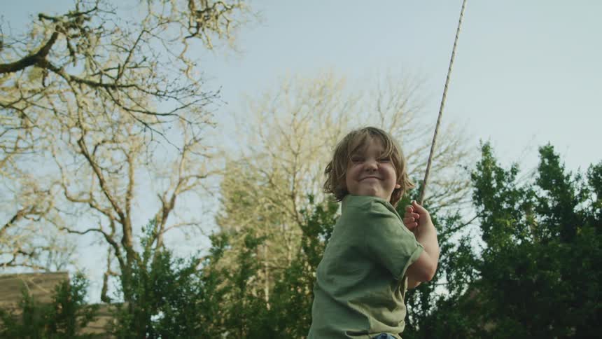 Boy smiles while swinging in field bordered by trees
