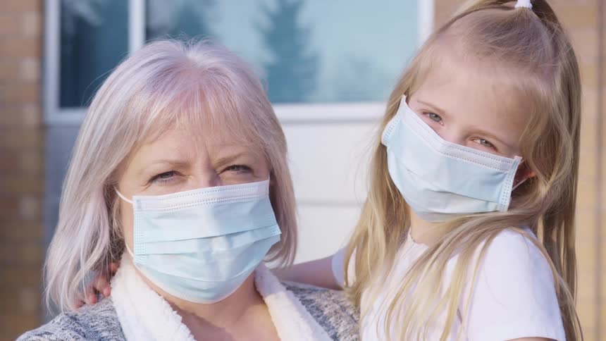 A grandmother holds her granddaughter while they both smile underneath disposable surgical face masks