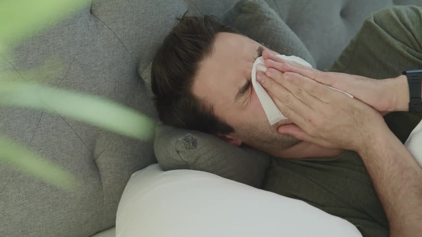 A man lying in bed blows his nose
