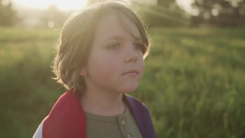 A child stands in a grassy field under the sun rays