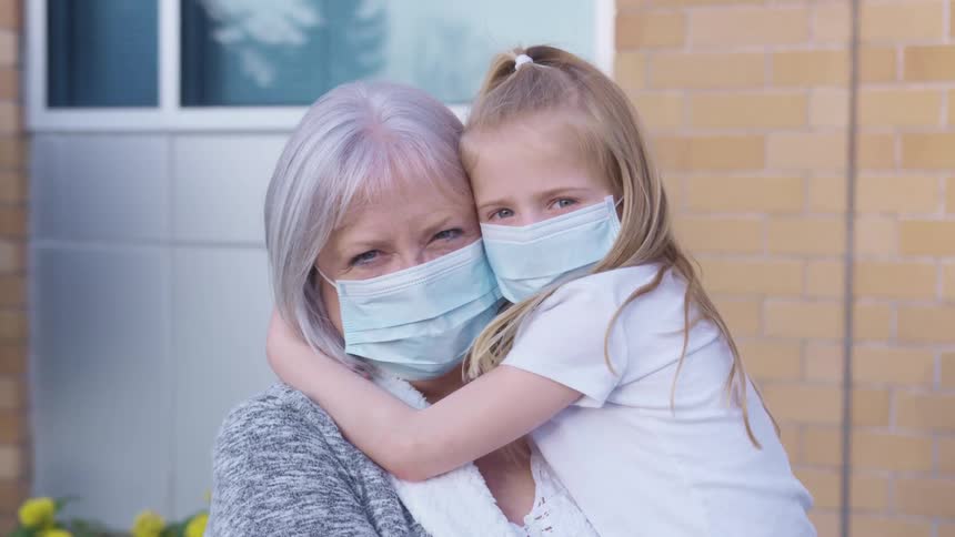 A little girl and her grandma hug and pose for a picture while wearing masks